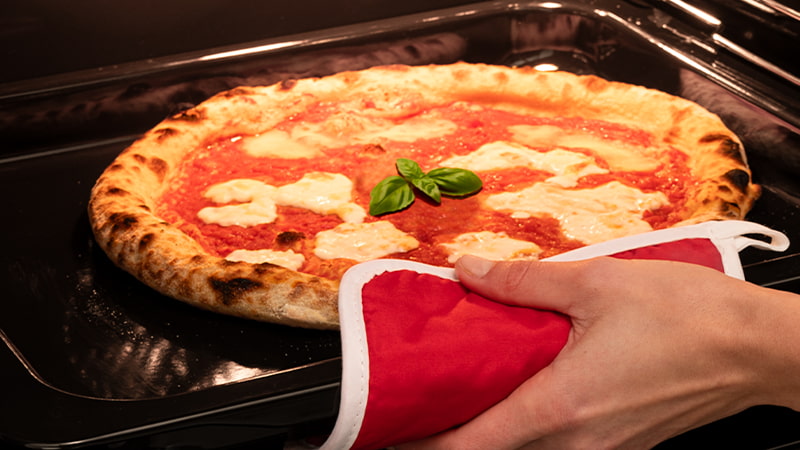 Pizza cotta in forno mentre una mano la estrae con una presina