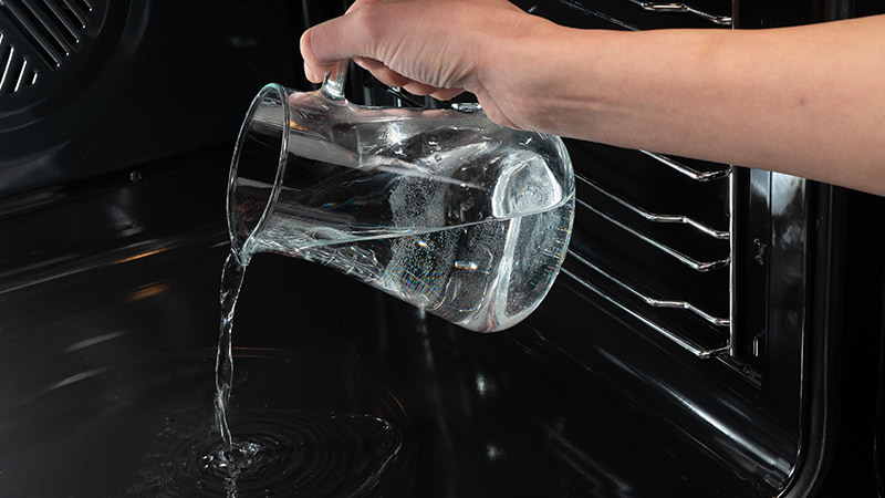 Acqua versata nel forno per la pulizia a vapore